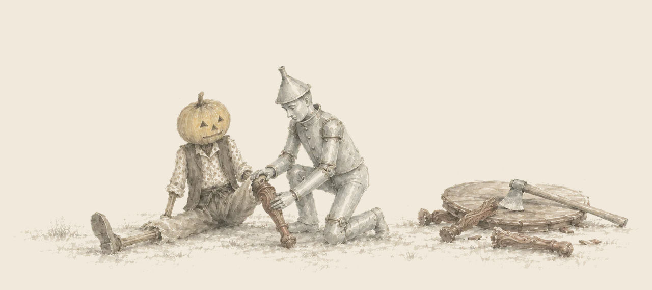 Jack Pumpkinhead sits on the ground with one leg while the Tin Woodman kneels fitting a carved table leg to the other; table pieces and an axe lie nearby.
