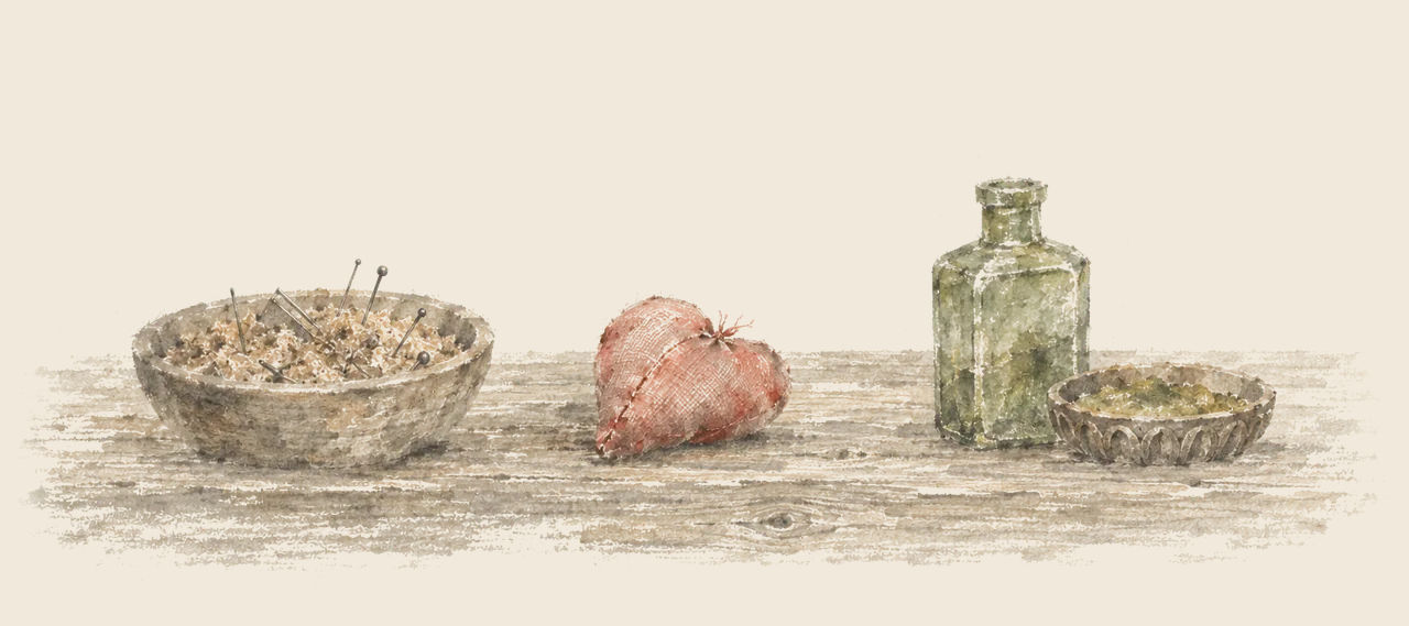 On a wooden table sit a bowl of bran full of pins and needles, a small silk heart, and a square green bottle beside a dish of green-gold.